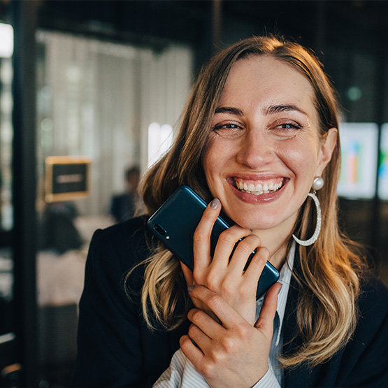 Glad kvinna håller en mobiltelefon och skrattar.